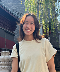 Briana Yang, LING 201 Peer mentor, is standing outside underneath willow tree, architecture in the background.