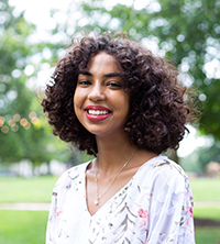 Sarah Bekele is an undergraduate teaching assistant for LING 190, she is outdoors bokeh lights, sky, and trees are in the background.