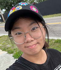 Talia Yu is a peer mentor for LING 201, she is among a landscape of trees, grass and sidewalk, smiling.